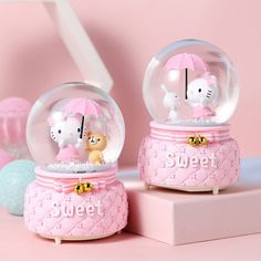 two hello kitty snow globes on top of a pink surface