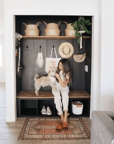 a woman holding a small white dog in front of a shelf with hats on it