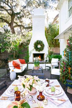 an outdoor table set with plates and fruit on it in front of a fire place