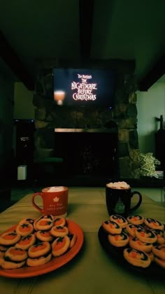 there are many donuts on the table with cups and mugs next to them