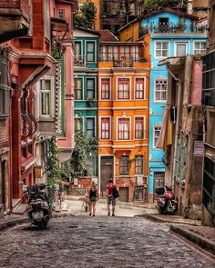 two people are walking down the street in front of some colorful buildings with balconies