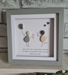 a white frame with two rocks in the shape of people holding hands and one has a balloon