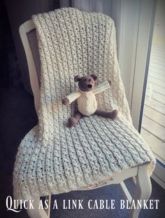 a teddy bear sitting on top of a white chair covered in a knitted blanket