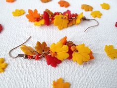 several pairs of earrings with autumn leaves on them sitting on a white cloth covered table