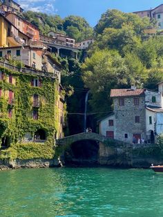 some buildings are on the side of a hill by water with a boat in it