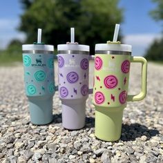 three different colored cups with straws in them sitting on the ground next to some rocks