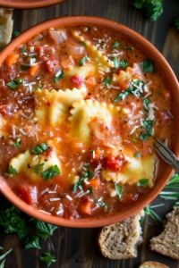 a bowl of pasta soup with bread and parsley on the side, ready to be eaten