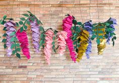 paper flowers hanging on a brick wall with green leaves and pink ones in the middle