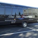 a black tour bus parked in front of a large glass building with its doors open