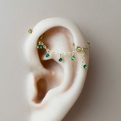 a pair of ear piercings with green stones on them sitting on top of a white surface