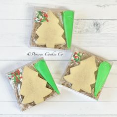 three christmas tree shaped cookies in plastic bags on a white wooden table with green ribbon