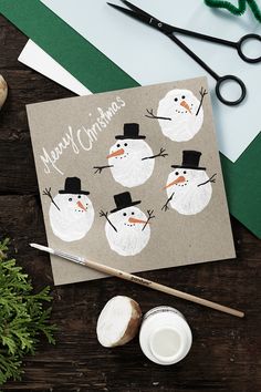 a christmas card with snowmen on it next to some scissors and other crafting supplies