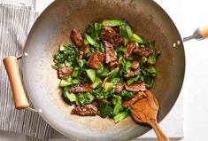 a pan filled with meat and vegetables on top of a stove next to a wooden spoon