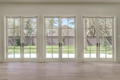 an empty living room with french doors leading to the back yard and large windows on both sides