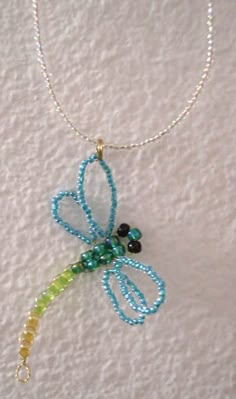 a beaded necklace with a dragonfly on it's end and beads hanging from the back