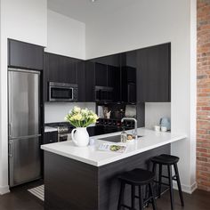 a kitchen with black cabinets and white counter tops, two stools at the island