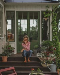 a woman sitting on steps in front of a house with potted plants next to her