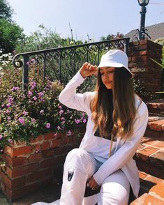 a woman sitting on the steps wearing white pants and a hat with her hands behind her head