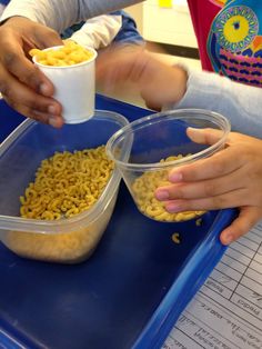 two children are eating cereal out of plastic containers on a blue tray with paper cups