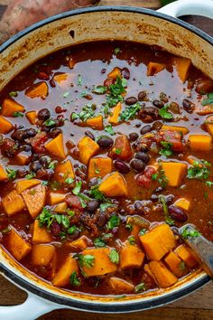 a pot filled with black beans and sweet potato soup on top of a wooden table