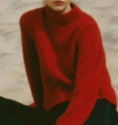 a woman sitting on the ground wearing a red sweater