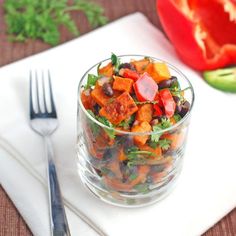 a glass bowl filled with vegetables next to a knife and fork on top of a white place mat