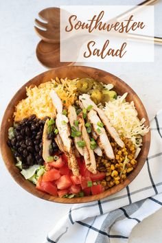 a wooden bowl filled with chicken, rice and beans next to two spoons on a white surface