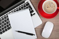 an open laptop computer sitting on top of a wooden desk next to a cup of coffee