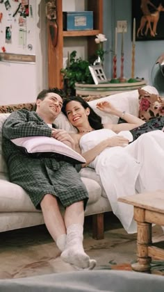 a man and woman laying on a couch in a living room with an open book