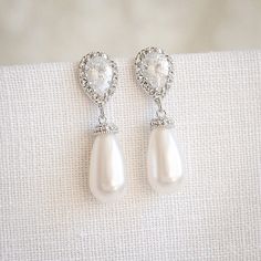 a pair of pearl and diamond earrings on a white cloth background, with the image of a heart in the center