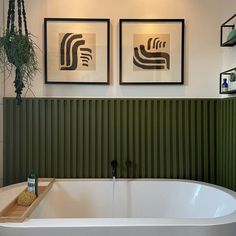 a bathroom with two framed pictures above the bathtub and on the wall is a plant