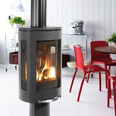 a fire place in the middle of a room with red chairs and tables around it