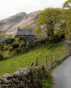 an old stone house sits on the side of a country road near a mountain range