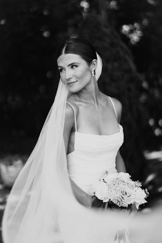 black and white photo of bride in wedding dress with veil over her head looking at camera