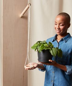 a woman is holding a potted plant on a string hanging from a hook and smiling at the camera