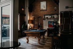 a pool table sitting in the middle of a living room next to a brick wall