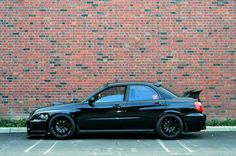 a black car parked in front of a brick wall