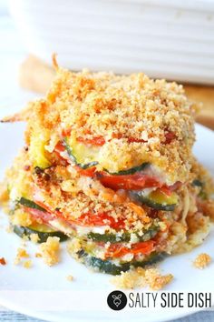 a stack of vegetable casserole on a white plate next to a baking dish