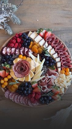 a platter filled with meats, cheeses and fruit on top of a wooden table