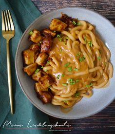 a plate with noodles, tofu and gravy on it next to a fork