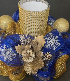 a blue and gold candle holder with snowflakes, pineconis and bells