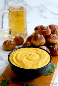 vegan beer cheese dip in a black bowl on a cutting board next to rolls