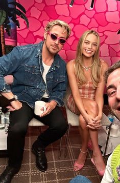 two men and a woman sitting next to each other in front of a pink wall