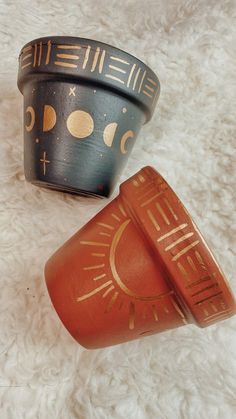 two small pots sitting on top of a white rug next to each other and one has a sun painted on it