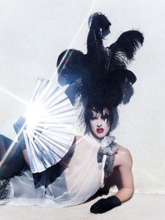 a woman laying on the ground with a fan in her hand and black feathers around her head