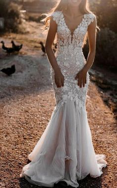 a woman in a wedding dress standing on a dirt road with birds flying around her