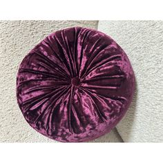 a purple velvet round pillow sitting on top of a white carpeted floor next to a wall