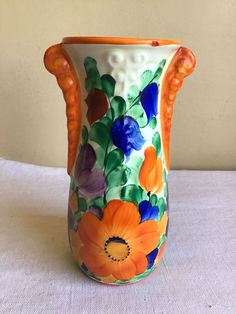 an orange and blue flowered vase on a white tablecloth with a wall in the background