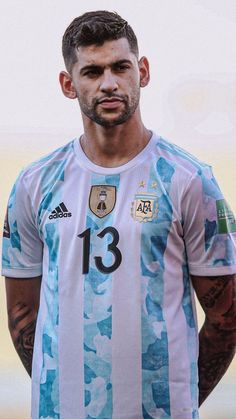 a man with tattoos standing in front of a white and blue soccer shirt that has stripes on it