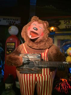 a man dressed as a clown holding a guitar in front of a carnival display at night